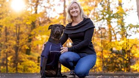 Caitlin Russell poses with her dog in front of fall leaves